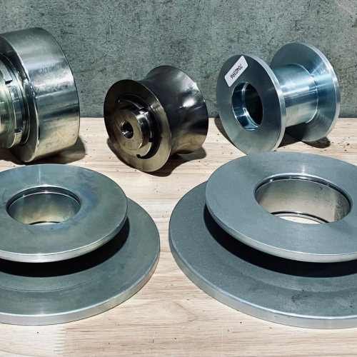 ONEMcDonough Several machined metal components, including discs and spools, are arranged on a wooden surface against a concrete background—ideal for use in elevator preventative maintenance.