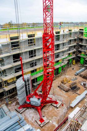 ONEMcDonough A large red construction crane from ONEMcDonough Elevators and Rentals stands in the middle of a building site, surrounded by scaffolding and construction materials, with a partially built multi-story structure in the background.
