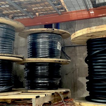 ONEMcDonough Large wooden spools holding coils of black cable, along with industrial elevator parts, are stacked on metal shelves in an industrial storage area.