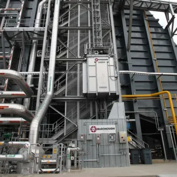 ONEMcDonough Industrial facility exterior with metal pipes, machinery, and a McDonough-branded service elevator mounted on a tall structure, ideal for conducting Elevator Drop Tests.