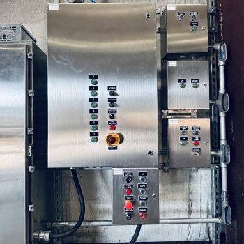 ONEMcDonough A stainless steel industrial control panel featuring multiple buttons, switches, indicator lights, and labels—often found alongside industrial elevator parts—mounted on a wall with visible conduit and wiring.