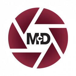 ONEMcDonough A maroon circular logo with segmented lines resembling a camera shutter, featuring the letters McD in bold black text at the center.