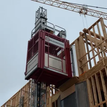 ONEMcDonough A commercial elevator rental is attached to a wooden building framework, with a crane and cloudy sky in the background.