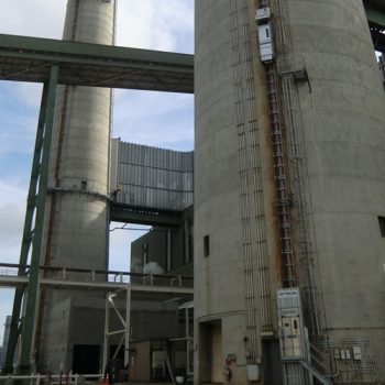 ONEMcDonough Large concrete industrial silos with external ladders and elevator, featuring elevator service and maintenance access, connected by elevated walkways and surrounded by metal structures.
