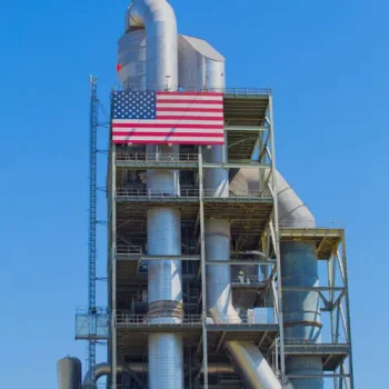 ONEMcDonough Industrial facility with metal pipes and structures against a clear blue sky, featuring a large American flag displayed on the upper section—ideal for Elevator Repairs and maintenance operations.