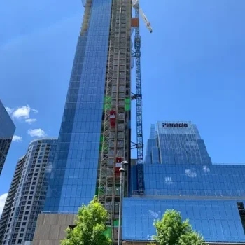 ONEMcDonough A tall glass skyscraper under construction with a crane and construction hoist rental beside it, set against a clear blue sky; a building labeled Pinnacle is visible in the background.